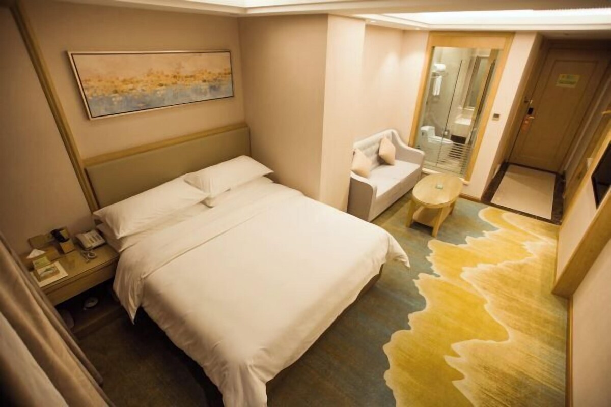 A hotel room with a bed, a chair, a small table, and a painting on the wall.