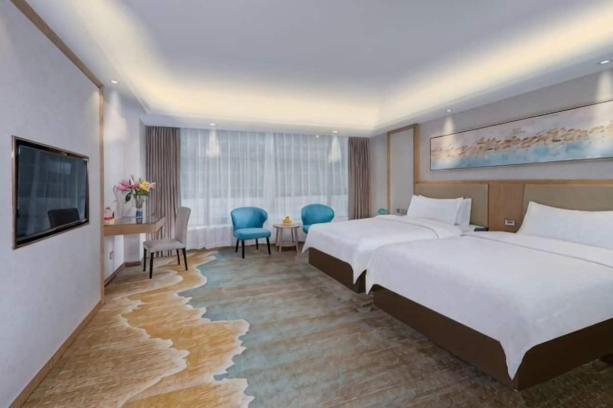 A hotel room with a bed, two chairs, a desk, a TV, and a large window with curtains.