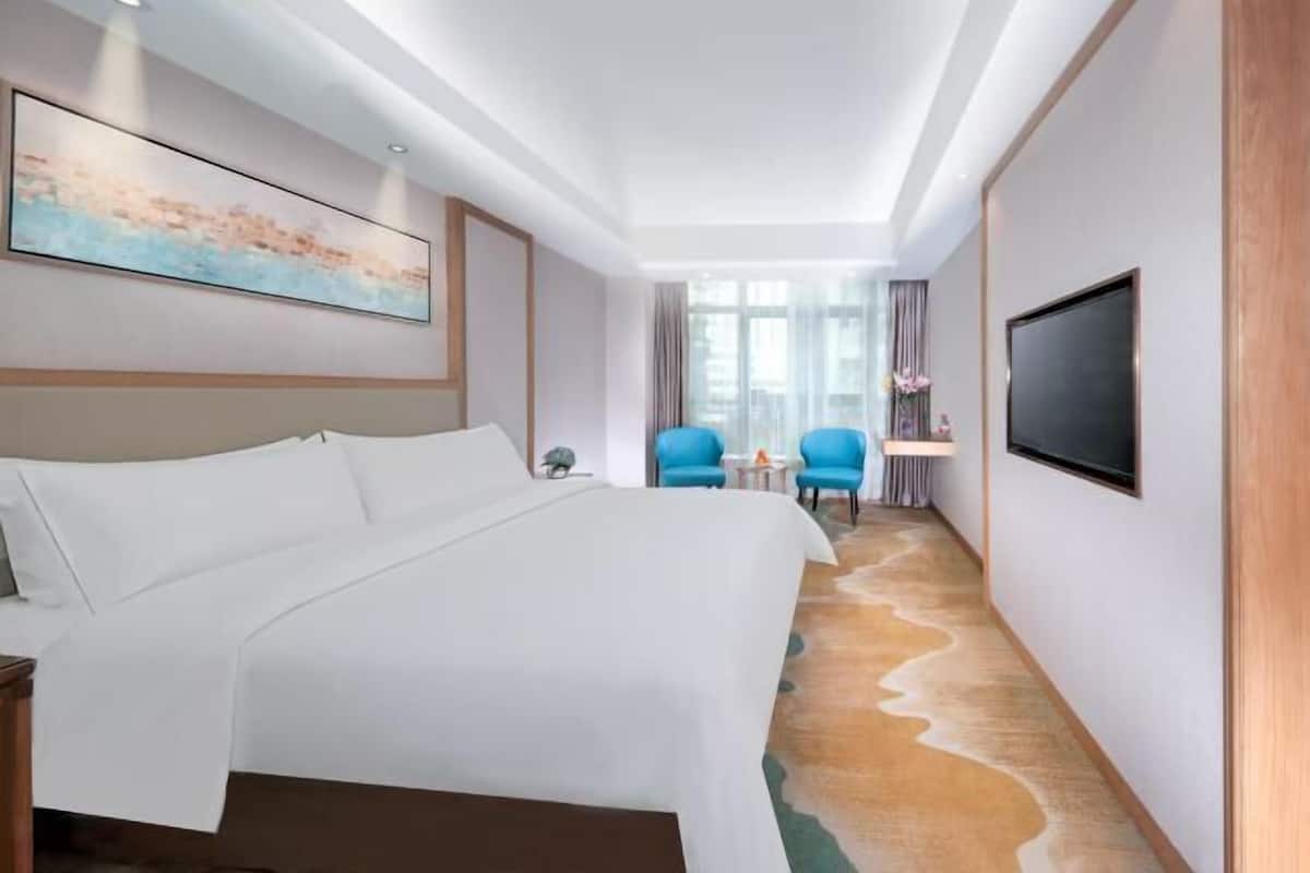 A hotel room with a large bed, a flat-screen TV, a painting on the wall, and a view of the hallway.