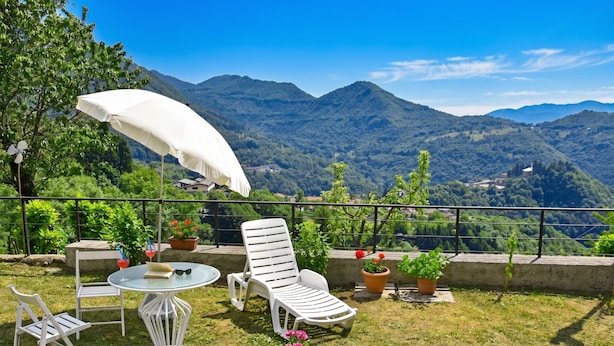 A terrace with a white umbrella, lounge chairs, and potted plants. - Casa Busso, Esino Lario, Italy (Esino Lario)