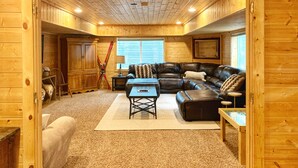 A log cabin interior with a leather sofa, a coffee table, and a ski rack. - Cozy Cabin Themed Basement (Morgan)