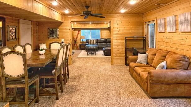 A wooden interior with a dining area, a living room, and a ceiling fan. - Cozy Cabin Themed Basement (Morgan)