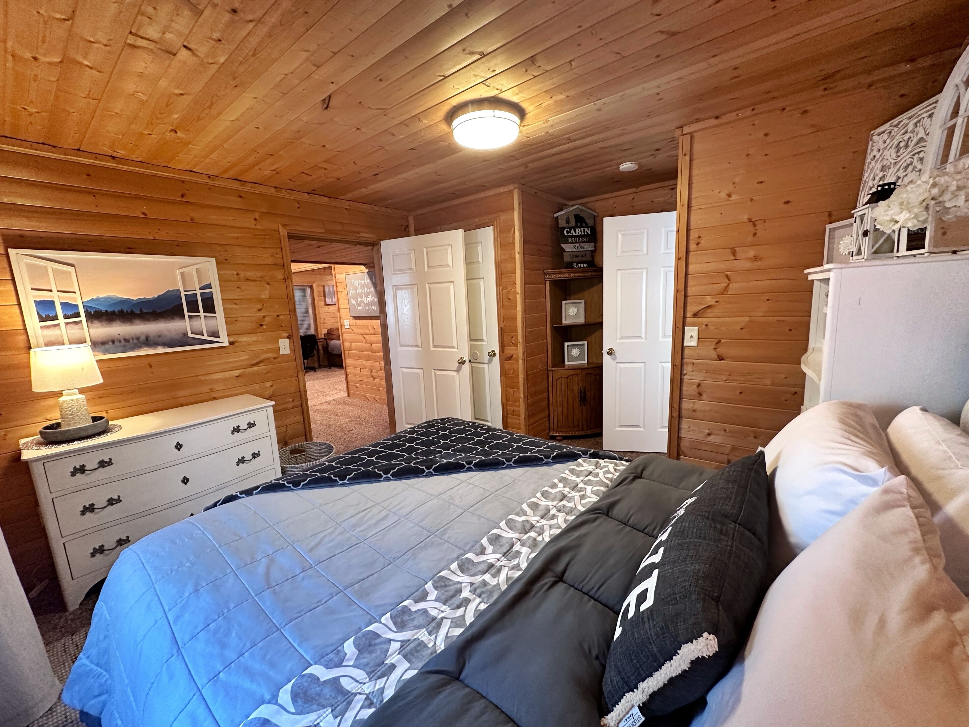 A wooden cabin bedroom with a bed, dresser, and a painting of a mountain landscape.