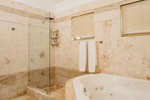 Un baño con ducha de vidrio, bañera y ventana con persianas.
