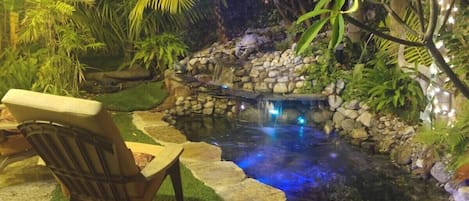 A garden with a pond, stone steps, and a chair.