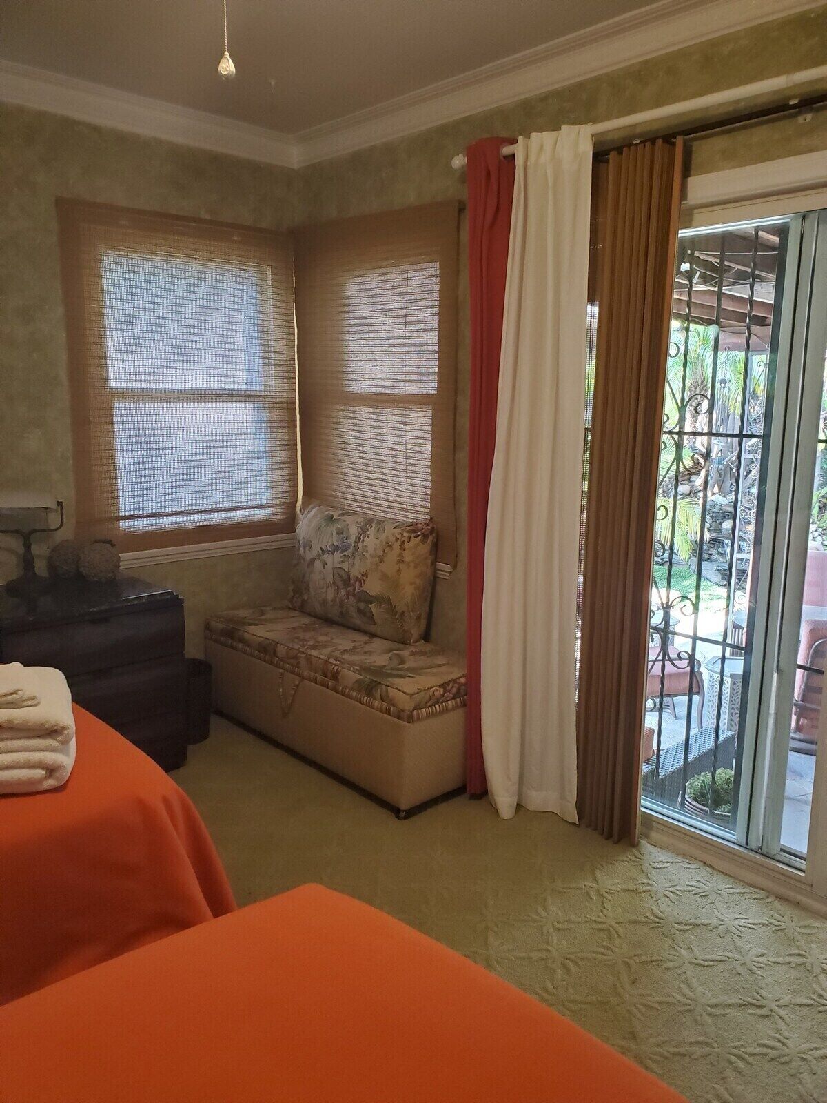Una habitación con cama, un banco, una mesita y una ventana con cortinas.