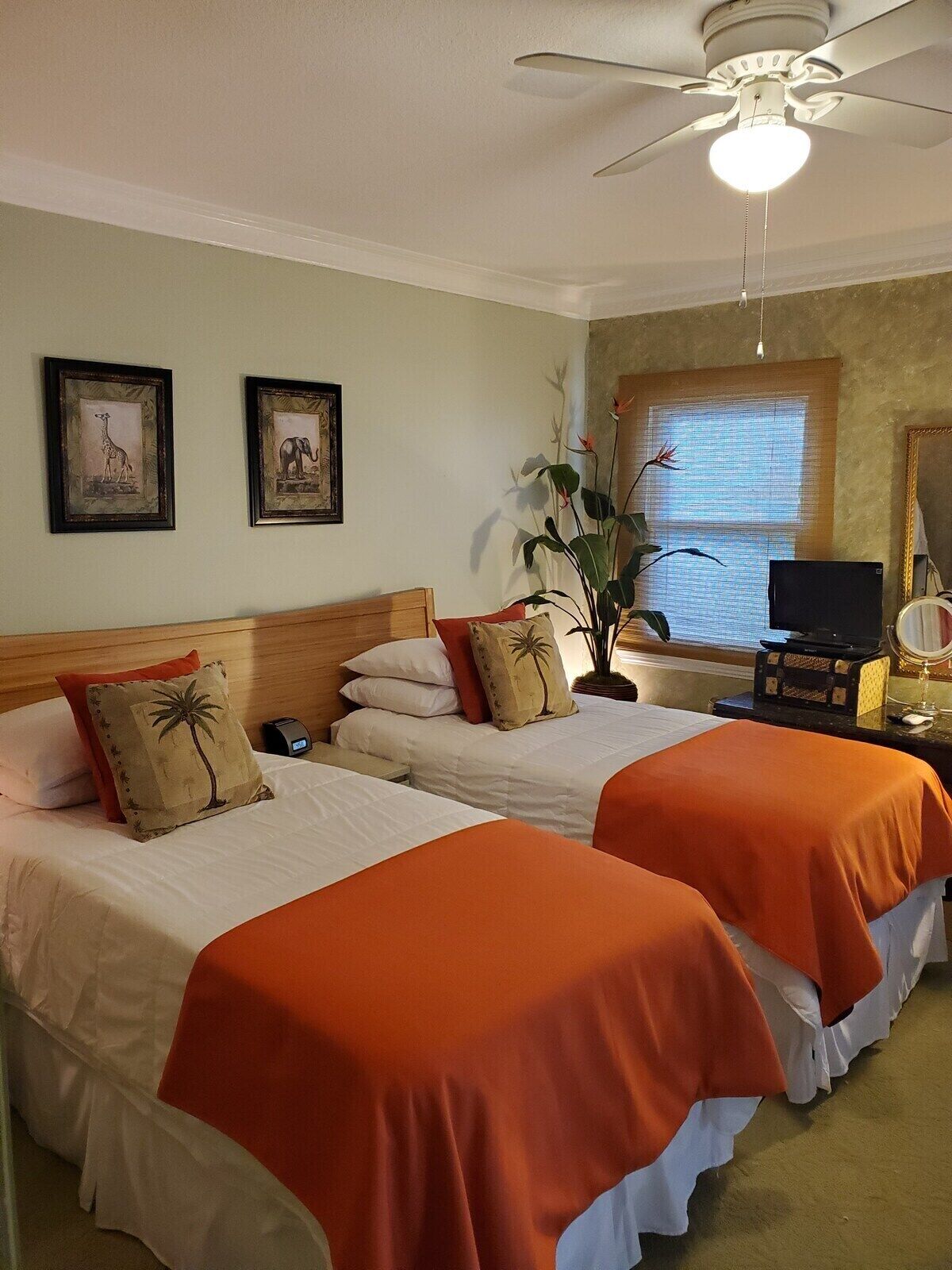 A hotel room with two beds, a ceiling fan, a large window with blinds, and a television.