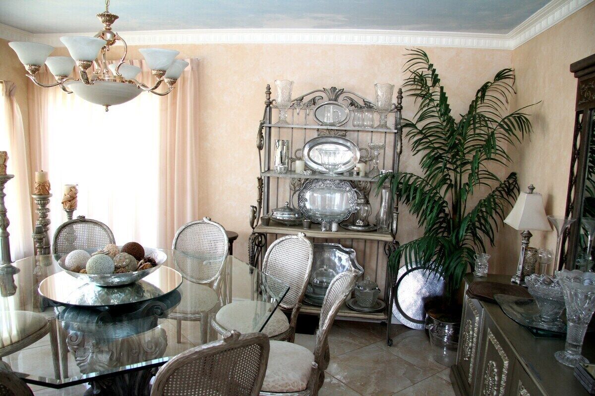 A dining area with a glass table, wicker chairs, a chandelier, and a display of silverware and glassware.