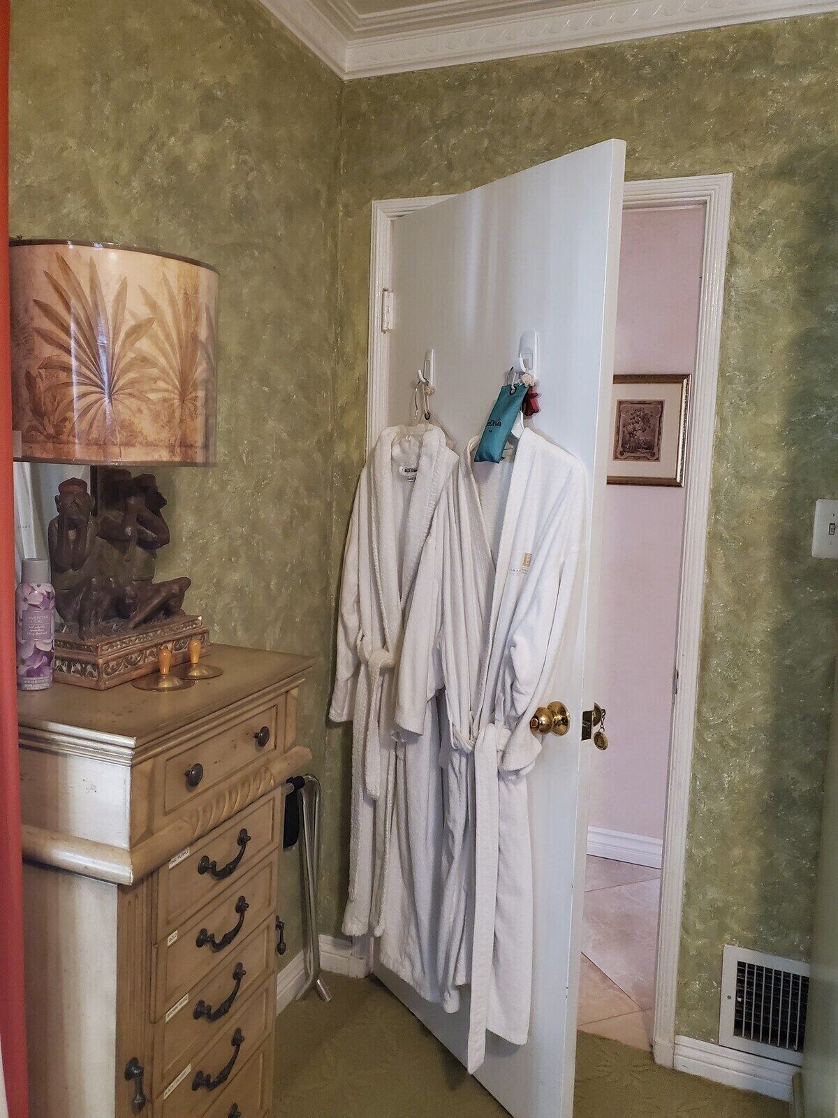A bathroom with a wooden dresser, a towel rack with robes, a decorative lamp, and a shower area.