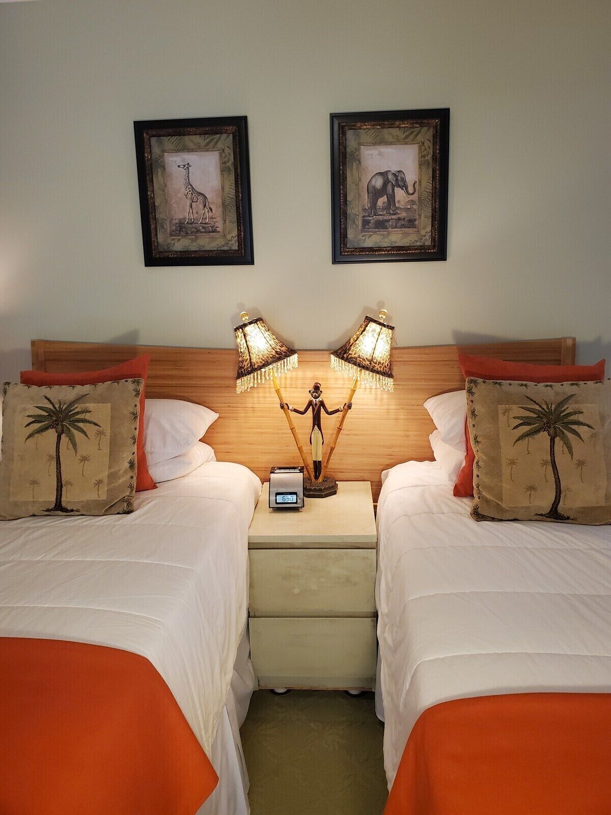 Una habitación de hotel con dos camas, una mesita de noche con un reloj y dos cuadros en la pared.