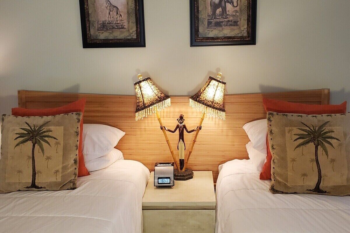 A hotel room with two beds, a nightstand with a clock, and two framed pictures on the wall.