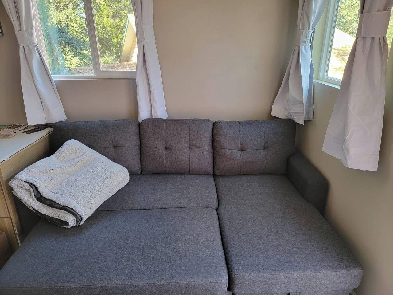 En grå sofa med et hvidt tæppe, et lille bord og gardiner foran et vindue.