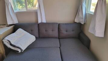 En grå sofa med et hvidt tæppe, et lille bord og gardiner foran et vindue.