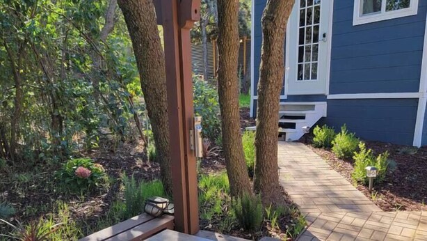 Un pati amb una llar de foc integrada, envoltat d'arbres i un camí que condueix a una casa.