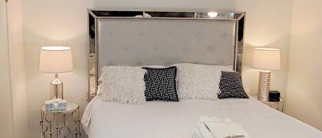 A neatly made bed with white linens, two patterned pillows, and a folded towel on the side. There are two bedside lamps on either side of the bed.