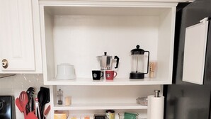 Eine Küche mit weißen Schränken, einer Holz Arbeitsplatte und verschiedenen Küchenutensilien, darunter eine Kaffeemaschine, Tassen und Teedosen.