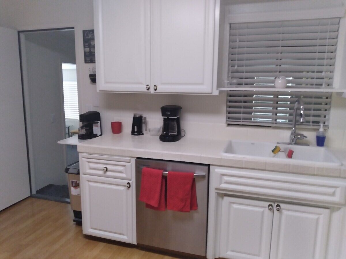 A kitchen with white cabinets, a countertop, a sink, and a dish drying rack.