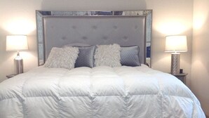 Ein großes Bett mit einem gepolsterten Kopfteil, zwei Nachttischlampen und einem Spiegel über dem Kopfteil.