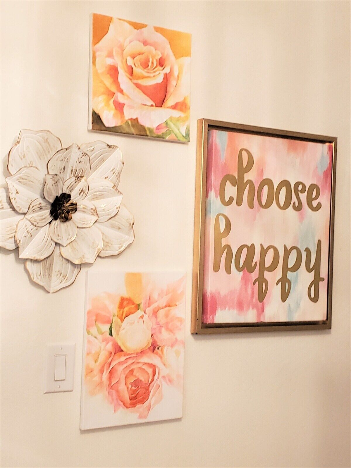 Un mur orné de trois œuvres d’art encadrées : une grande fleur blanche, une rose à l’aquarelle aux tons rose et orange, et une pancarte encadrée sur laquelle on peut lire : « Choisissez le bonheur ».