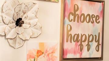 Un mur orné de trois œuvres d’art encadrées : une grande fleur blanche, une rose à l’aquarelle aux tons rose et orange, et une pancarte encadrée sur laquelle on peut lire : « Choisissez le bonheur ».