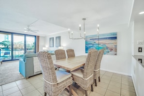 A dining area with a wooden table and wicker chairs, a ceiling fan, and a painting of a beach scene.