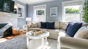 A living room with a beige sofa, a glass coffee table, a fireplace, and a television. - USNA Home Steps to Stadium Dog-Friendly w Parking (Annapolis)