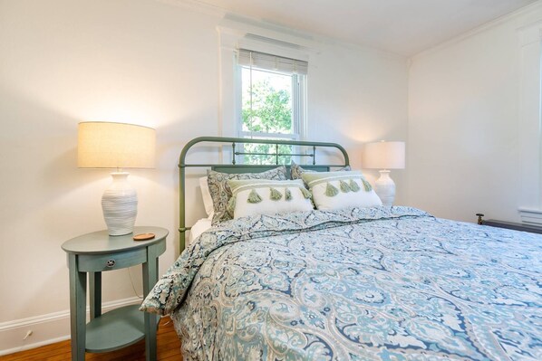 Une chambre à coucher avec un lit, deux tables de chevet, une fenêtre et une petite table.