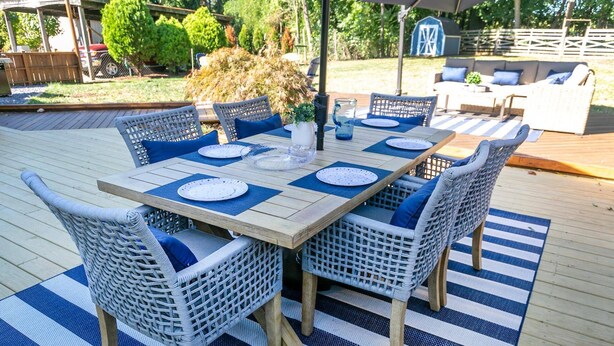 A wooden deck with a rectangular table set for four, surrounded by wicker chairs with blue cushions. - USNA Home Steps to Stadium Dog-Friendly w Parking (Annapolis)