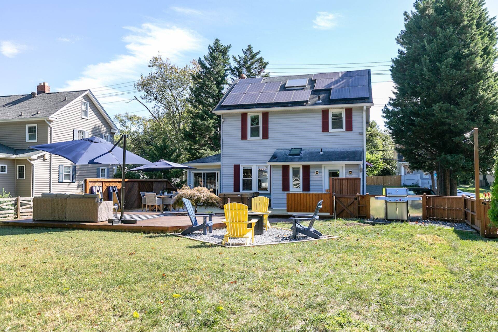Ein zweistöckiges Haus mit Hinterhof-Terrasse, Gartenmöbeln und einem Grill.