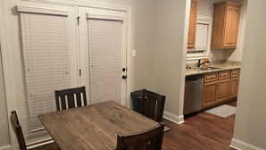 Un comedor con mesa y sillas de madera, una cocina con armarios de madera y un lavavajillas, y una puerta blanca con persianas.