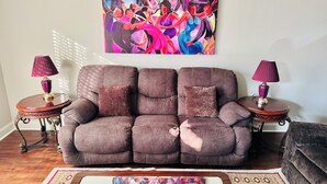 Una sala de estar con un sofá marrón, dos mesitas de noche con lámparas, un cuadro abstracto colorido y una alfombra estampada.