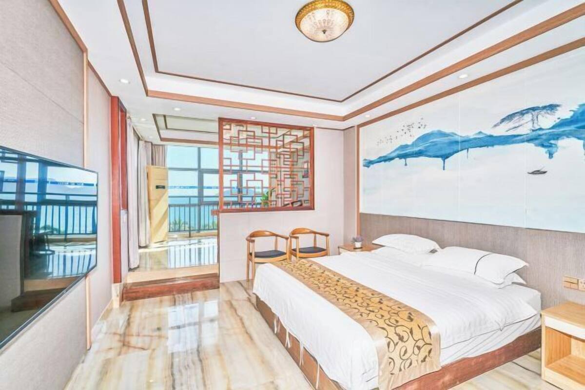 A hotel room with a large bed, a TV, a decorative screen, and a view of the outdoors.