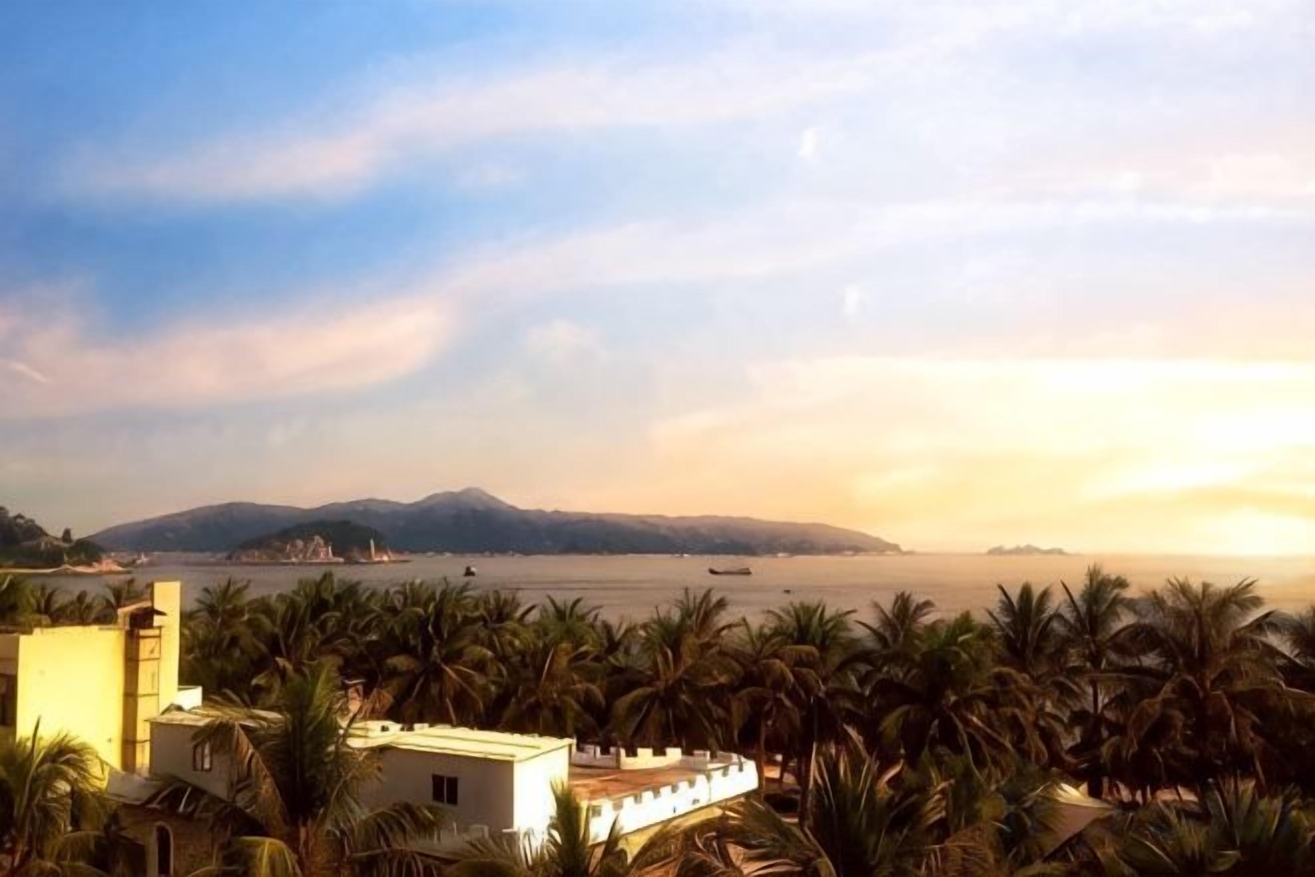 A coastal view with palm trees and a building in the foreground.