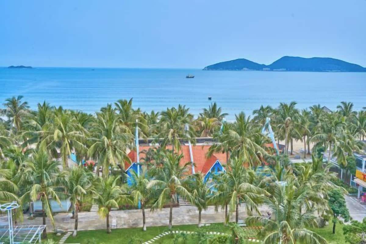 A coastal view with palm trees, a beach, and a distant mountain range.