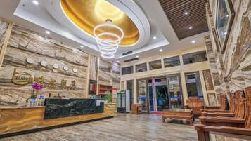 A hotel lobby with a reception desk, seating area, and a large chandelier.