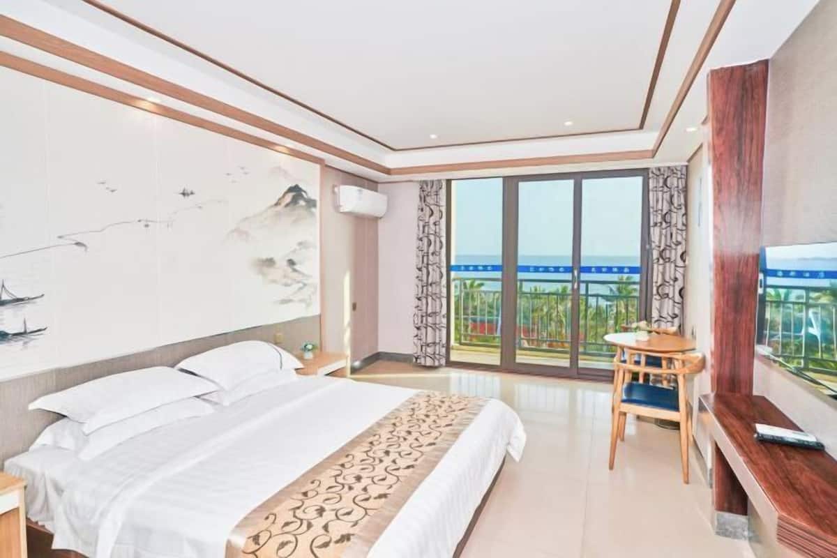 A hotel room with a large bed, a small table, a TV, and a balcony with a view.