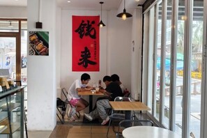 A restaurant interior with a group of people dining at a table, a large red banner on the wall, and a view through the window. - Haidu Hotel (Taishan)