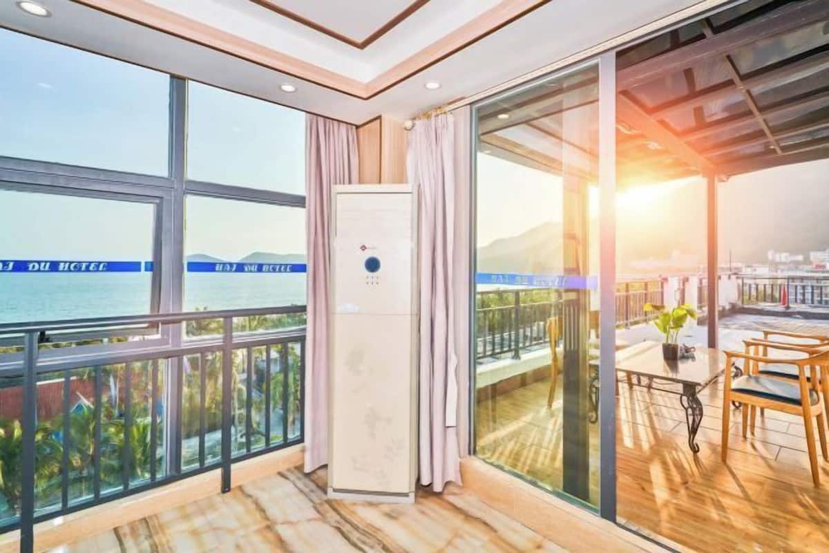 A balcony with a view of the sea, a table with chairs, and a large window with curtains.