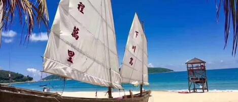 A boat with sails on a beach, a lifeguard tower, and clear blue water.