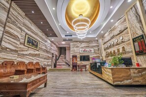 A hotel lobby with a reception desk, wooden seating, a staircase, and a marble wall. - Haidu Hotel (Taishan)