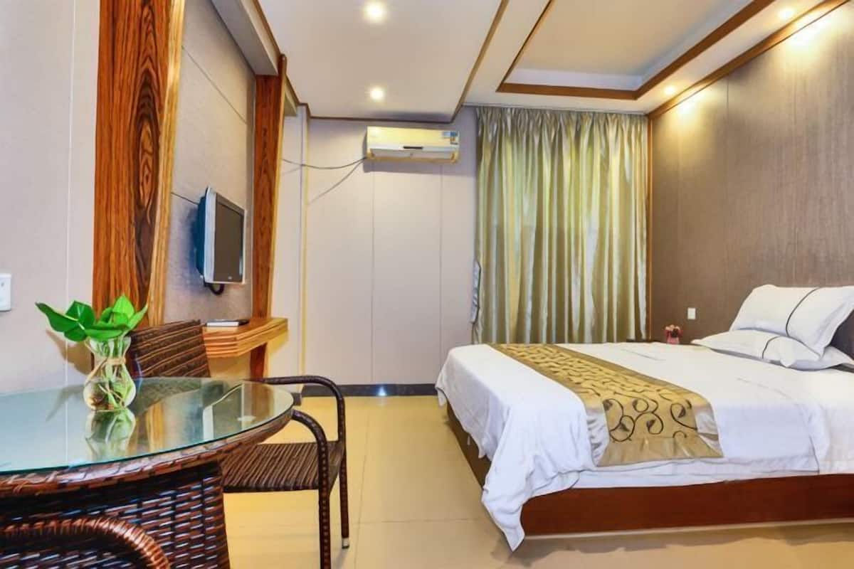 A hotel room with a bed, a glass table with chairs, a TV, and an air conditioning unit.