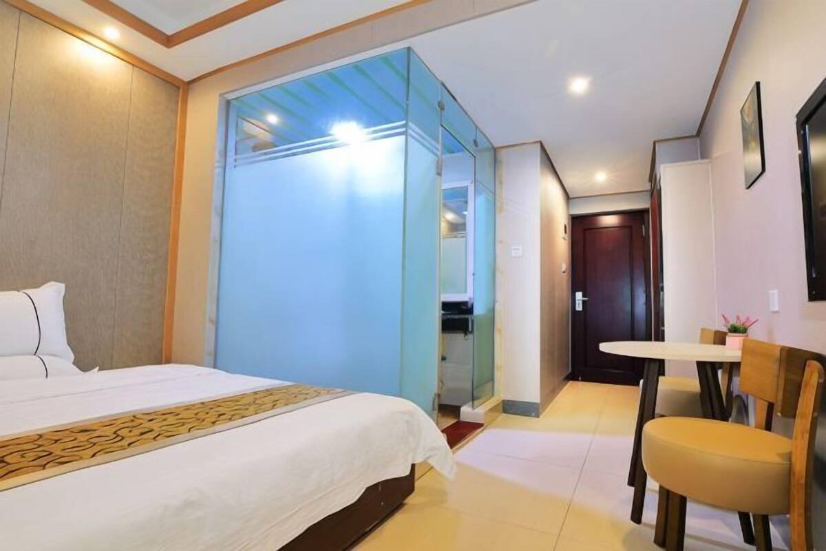 A hotel room with a bed, a desk, a chair, and a glass partition.