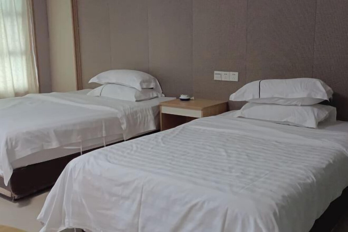 A hotel room with two single beds, a wooden nightstand, and a wall socket.