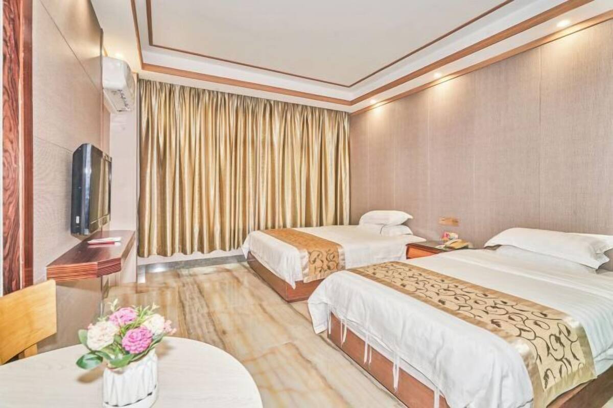 A hotel room with two beds, a TV, a desk, and a dining table with flowers.