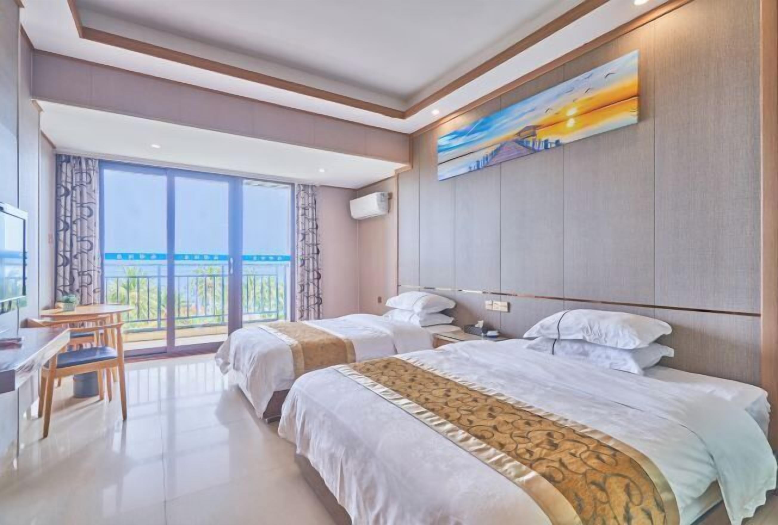 A hotel room with two beds, a desk, and a large window with a view.