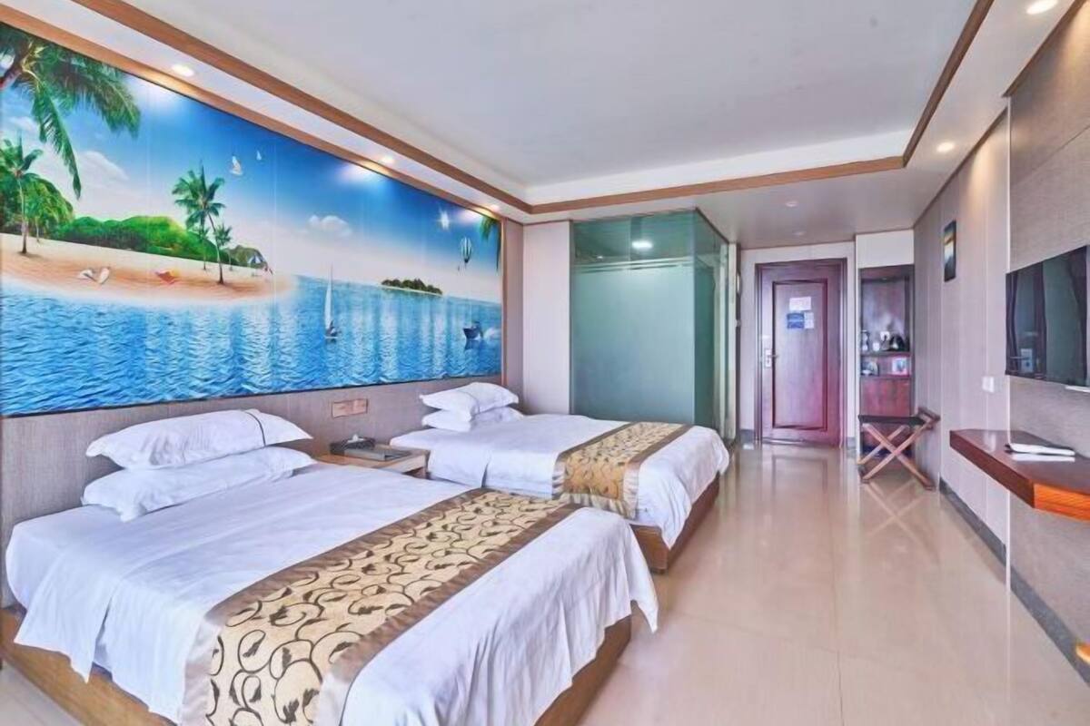 A hotel room with two beds, a mural of a beach scene, a TV, and a reception desk.