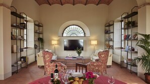 A spacious living room with a high ceiling, a large arched window, and a fireplace. There are two sofas, a coffee table, and bookshelves filled with books and decorative items. - Casa Lionardo - House with private pool (Vinci)