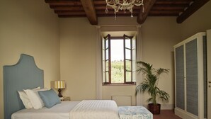 A bedroom with a large bed, a nightstand, a lamp, a window with a view, a potted plant, and a wardrobe. - Casa Lionardo - House with private pool (Vinci)