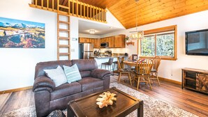 A cozy living room with a brown leather sofa, wooden dining table, and a kitchen in the background.