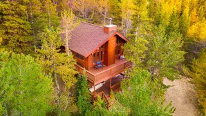 A wooden cabin with a balcony, surrounded by dense forest.